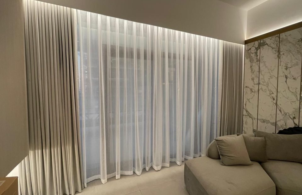 A photo of a modern bedroom with a large bed and a dresser. The room has a high ceiling with a circular light fixture and a large window with sheer curtains. The curtains let in natural light and create a soft, airy atmosphere in the room.